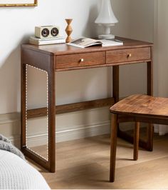 a wooden desk with two drawers and a lamp next to it in a room that has white walls