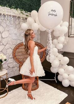 a woman in a short white dress standing next to balloons