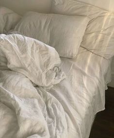 an unmade bed with white sheets and pillows