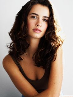 a beautiful young woman sitting on top of a wooden table next to a white wall