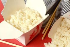 rice in a box with chopsticks next to it on a red tablecloth