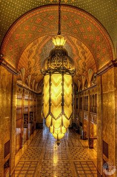 an ornate hallway in a building with gold and black tiles on the floor, chandelier hanging from the ceiling