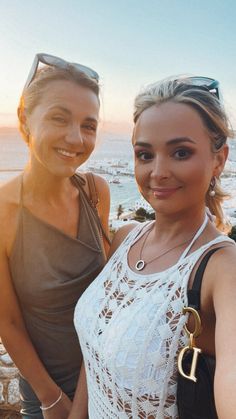 two beautiful women standing next to each other in front of the ocean with sunglasses on