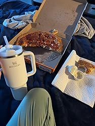 a person sitting on a bed with pizza and drinks