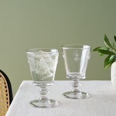 two glass goblets sitting on top of a table next to a potted plant