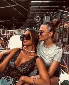 two beautiful women sitting next to each other at an outdoor table covered in umbrellas