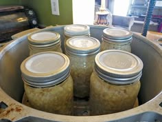 six jars filled with pickles sitting in a metal container on top of a table