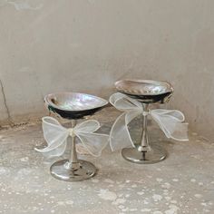 two silver candlesticks with bows on them sitting next to each other in front of a wall