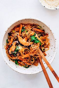 a white bowl filled with noodles and vegetables next to chopsticks on a table