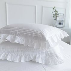 two pillows stacked on top of each other on a bed with white sheets and ruffles