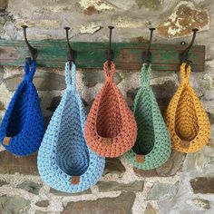 four crocheted purses hanging from hooks on a stone wall