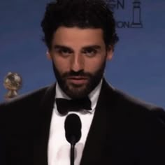 a bearded man in a tuxedo holding a microphone