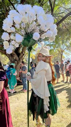 a woman dressed in costume standing next to a tall white flower plant with lots of flowers on it