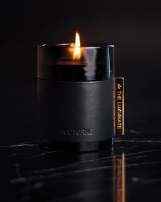 a lit candle sitting on top of a table next to a black container with writing