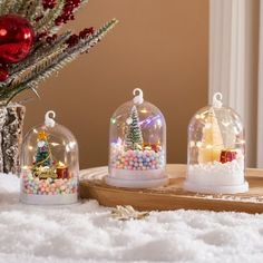 three snow globes sitting on top of a wooden table next to a christmas tree