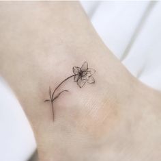 a small flower tattoo on the ankle is shown in black ink, and has a thin line drawing of a single flower