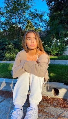 a woman sitting on the ground with her arms crossed and looking at the camera while wearing white sneakers