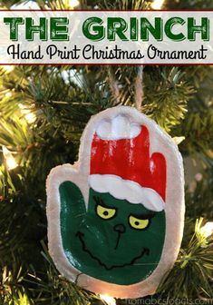 the grinch hand print christmas ornament hanging from a tree with text overlay