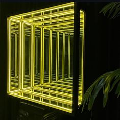 a yellow light that is inside of a black box in the dark with some plants around it