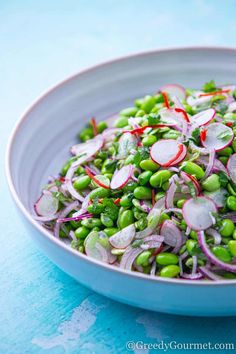 a white bowl filled with peas and radishes on top of a blue table