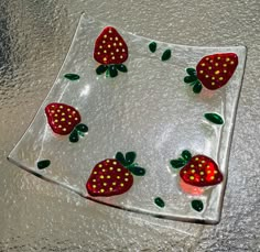 a glass plate with strawberries on it and green leaves in the center, sitting on a shiny surface