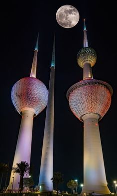 two very tall towers with some lights on them and the moon in the sky behind them