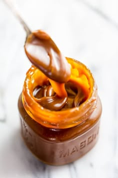 a spoon full of peanut butter and caramel on top of a jar filled with peanut butter