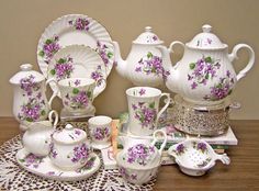 a table topped with lots of white dishes covered in purple and green flowered china