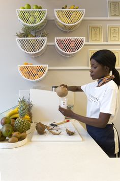 a woman standing in front of a counter holding a blender with fruit on it