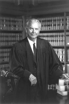 an old photo of a man in a robe and tie sitting at a desk with books