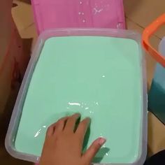 a child's hand touching the bottom of a plastic tray with green liquid on it