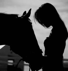 a woman standing next to a horse with her hand on it's bridle