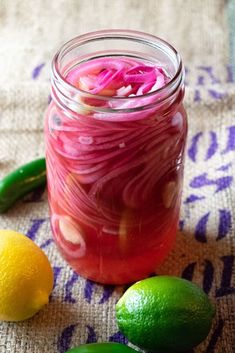 a mason jar filled with pickled onions next to lemons and lime wedges