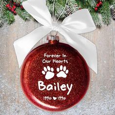 a red ornament hanging from a christmas tree with white ribbon and paw prints on it