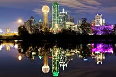 the city skyline is lit up at night with its lights reflecting in the still water