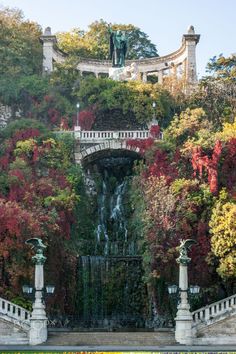 a waterfall in the middle of a lush green park with trees and bushes surrounding it