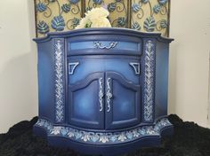 a blue cabinet with flowers on top and black furnishing behind it in front of a wall