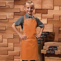 a young boy wearing an orange apron standing in front of stacks of pizza boxes with his hands on his hips