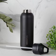 a black insulated water bottle next to a green plant on a marble countertop