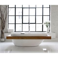 a white bath tub sitting under a window next to a wooden table with vases on it