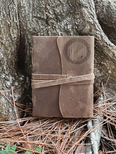 a brown leather journal sitting on the ground next to a tree