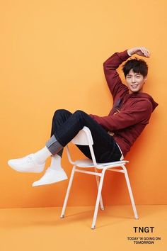 a man sitting on top of a white chair in front of an orange and yellow background