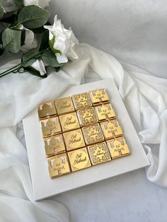 there is a bouquet of flowers next to some gold squares on a white cloth with the word love spelled in cursive writing