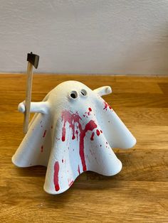 a white plastic ghost with blood on it holding a toothbrush in its mouth and standing on a wooden surface