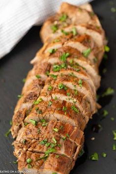 sliced pork on a black plate with parsley sprinkled around the top and sides