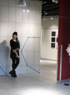 a woman standing next to a white wall