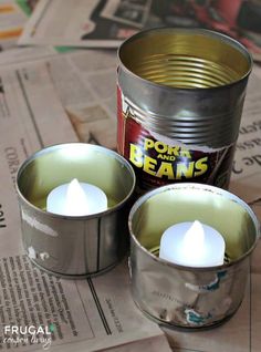 two tin can candles sitting next to each other on top of newspaper pages and paper