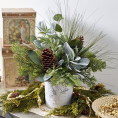 a vase filled with greenery and pine cones on top of a wooden table next to other items