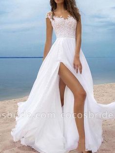 a woman standing on top of a sandy beach wearing a white dress and high heels