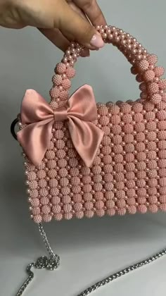 a hand holding a pink purse with a bow on the handle and chain attached to it